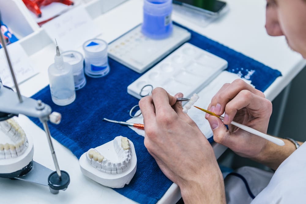Dental Technician Working on Models - Prosthodontics Dentistry A dental technician carefully shapes and customizes artificial teeth on dental models in a lab setting. - Prosthodontics Dentistry