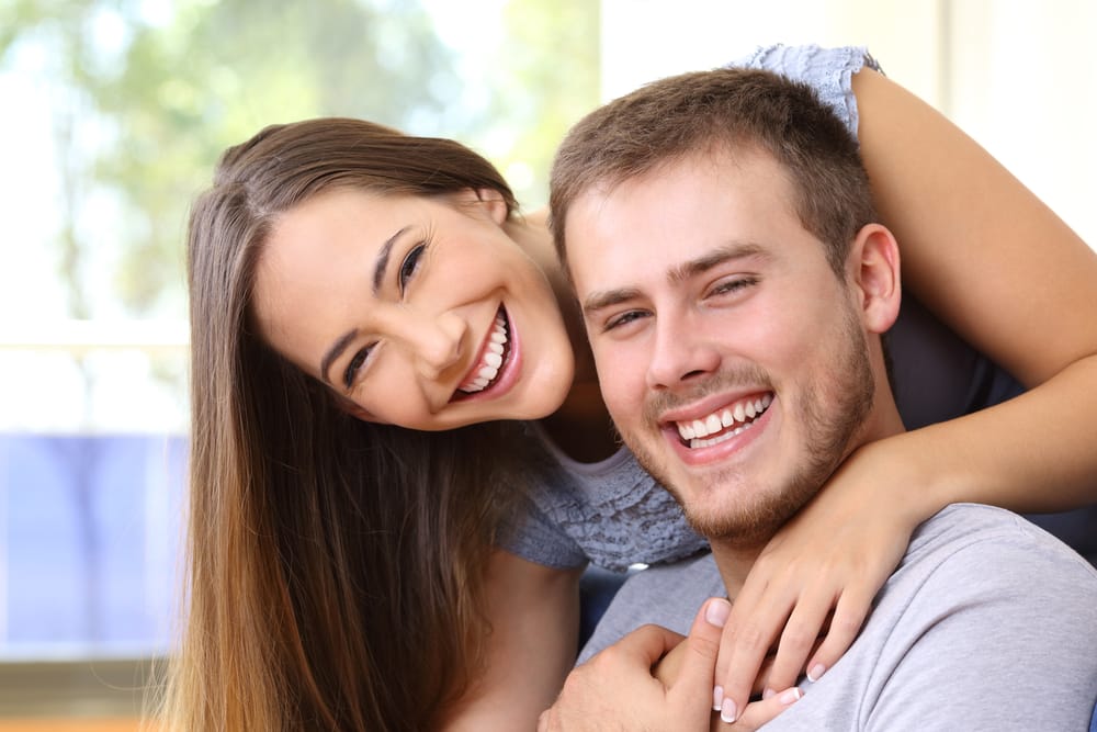 A young couple smiles brightly, embracing each other and looking cheerful. - Orthodontics