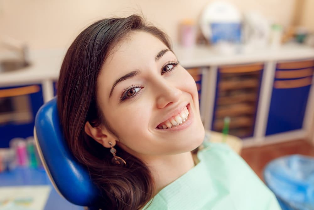 Smiling Woman in Dental Chair - Oral Surgery A young woman sits in a dental chair, smiling confidently after her dental checkup. - Oral Surgery