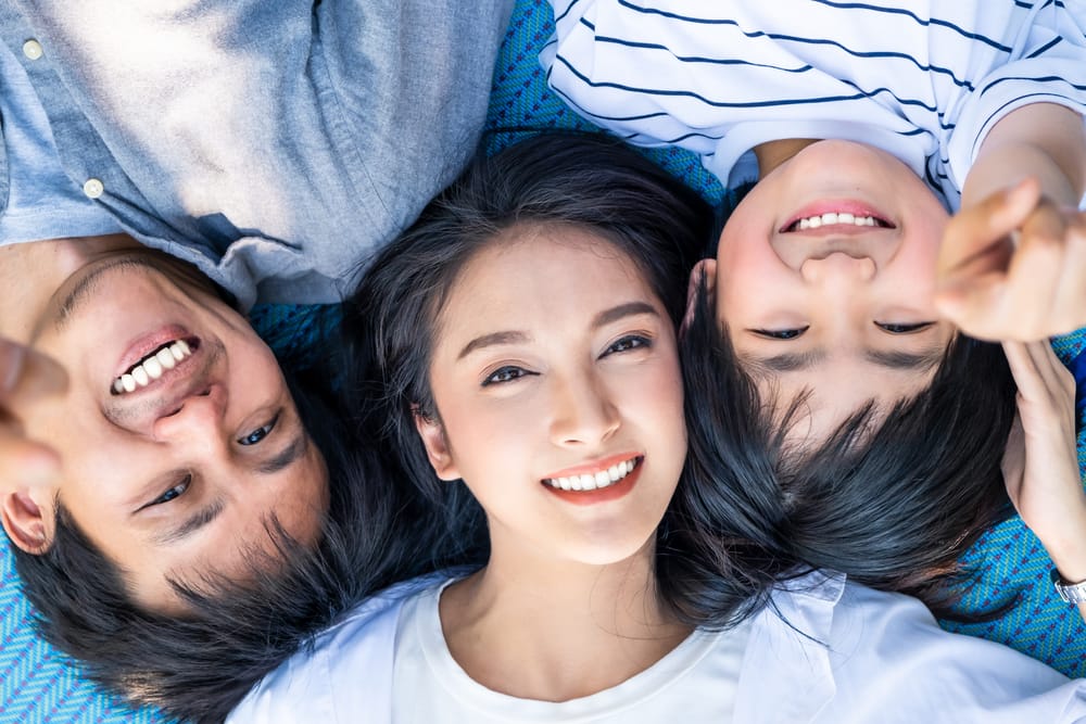 Happy Family Smiling Together - Dental Implants in West Palm beach Smiling family lying on a blanket together, enjoying time outdoors. - Dental Implants in West Palm beach